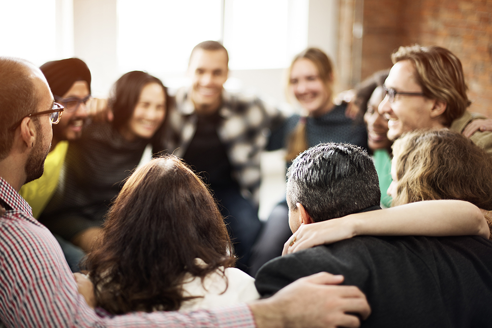 Group of people standing in a circle with their arms around one another's shoulders