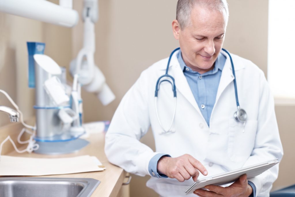 A mature dentist working on a digital tablet