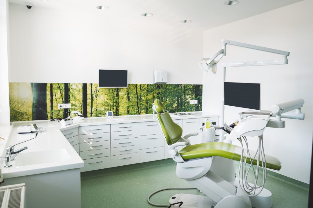 Empty brightly lit place of work of a dentist, modern dentist office with green dentist's chair, no people