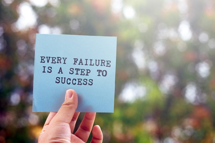 Hand holding inspirational message on paper, reading Every Failure is a Step to Success